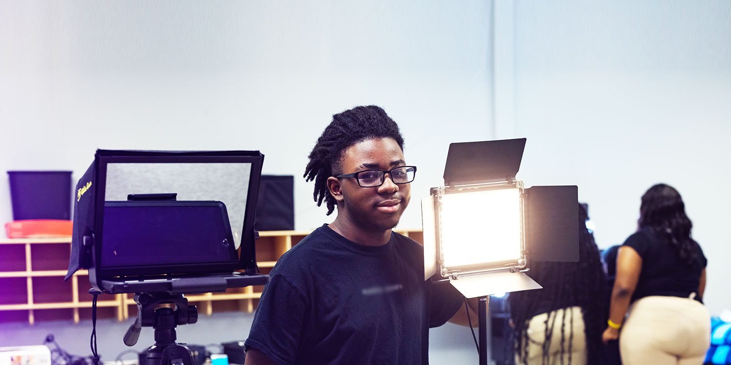 A student stands next to the light in the studio classroom, smiling.